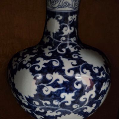 Chinese blue and white porcelain vase featuring an intricate scroll and floral motif, displayed on a dark wooden stand.