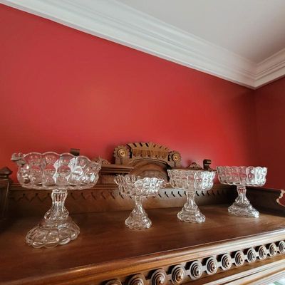 Four vintage clear pressed glass pedestal bowls in varying sizes, displayed on a wooden sideboard.