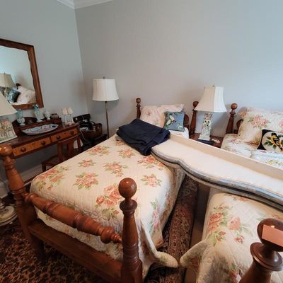 Pair of vintage colonial-style maple twin beds with turned posts, dressed in floral quilts, shown alongside a matching vanity with mirror...