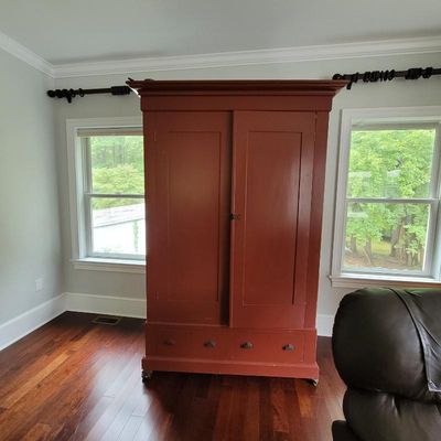 Large antique wooden armoire painted in a rustic red finish, featuring two tall doors over two bottom drawers with metal pulls.
