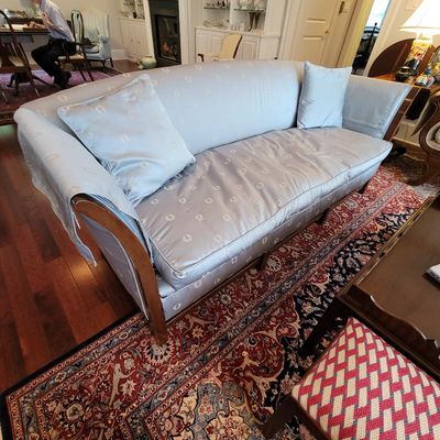 Traditional camelback sofa upholstered in a light blue patterned damask fabric, featuring matching throw pillows and arm covers.
