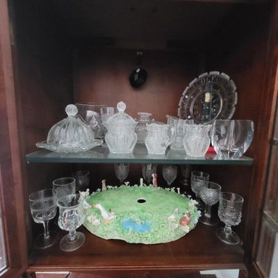 Collection of vintage pressed and cut glassware, including a covered butter dish, sugar bowl, creamers, and stemware, displayed alongside...
