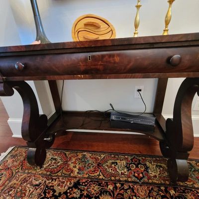 Antique Empire-style mahogany console table featuring a single drawer with wooden knobs, a keyhole, and ornate scroll-cut legs.