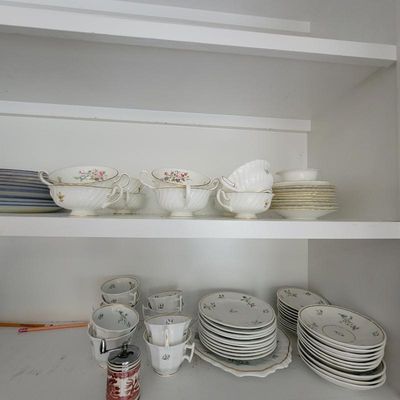 Assorted vintage fine china tableware, including floral-patterned teacups, saucers, and small plates with gold-rimmed detailing, arranged...