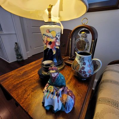 Assorted vintage collectibles on a wooden side table, including a Royal Doulton "The Ribbon Seller" figurine, a floral ceramic...