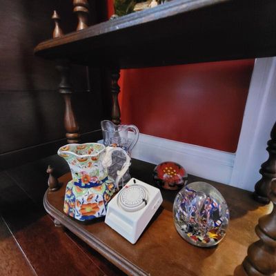 Assorted vintage collectibles displayed on a wooden shelf, including a floral ceramic pitcher, a clear cut-glass pitcher, two glass...