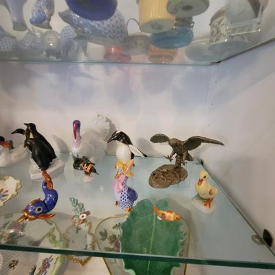 Collection of vintage porcelain and ceramic animal figurines, including penguins, a turkey, an eagle, and a duck, displayed on glass...