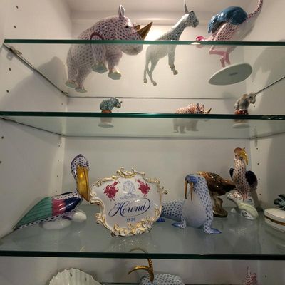 Collection of Herend hand-painted porcelain animal figurines, featuring their signature fishnet pattern, displayed on glass shelves with...