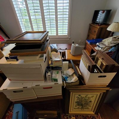 Assorted framed artwork, medical supplies, and household items packed in cardboard storage boxes.