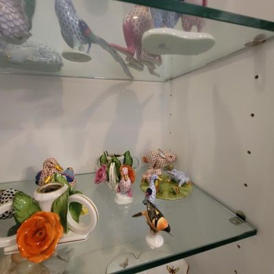 Collection of Herend porcelain figurines, including various birds, a rabbit, and floral-themed pieces, displayed on glass shelving.