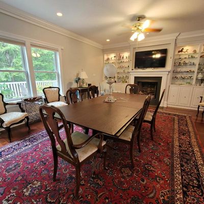 Traditional dark wood dining table with matching upholstered chairs, set over a large red patterned oriental rug in a well-lit dining room.