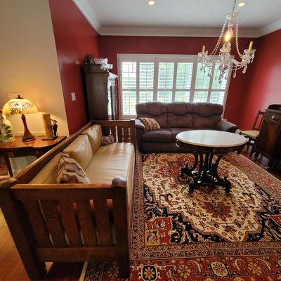 Mission-style oak daybed with tan cushions, paired with a Victorian-style marble-top parlor table and a large patterned area rug in a...