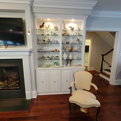 Built-in white display cabinet with glass shelves housing a collection of porcelain figurines and tea sets, paired with a French...