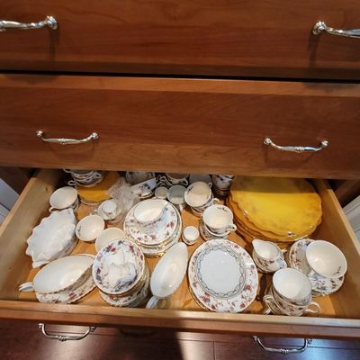 Assorted vintage fine china dinnerware, including floral teacups, saucers, serving dishes, and yellow plates, stored inside a wooden drawer.