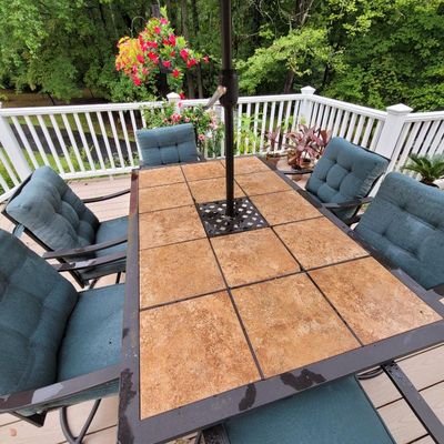 Outdoor dining set featuring a rectangular tile-top table with an umbrella hole, paired with six metal-framed armchairs with blue tufted...