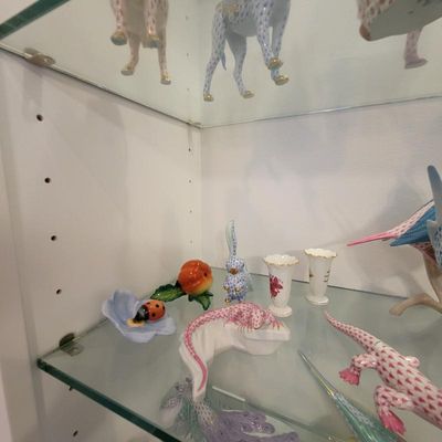 Collection of Herend porcelain figurines, including a pink fishnet lizard, a blue fishnet rabbit, and a ladybug on a flower, displayed on...