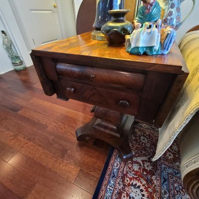 Antique Empire-style mahogany drop-leaf work table featuring two drawers, a pedestal base, and curved feet.