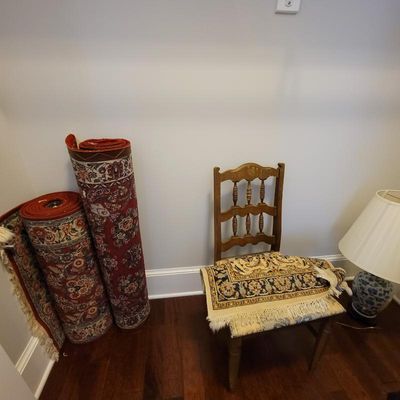 Two rolled Persian-style area rugs with red and cream floral patterns, shown alongside a ladder-back wooden chair and a blue and white...