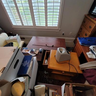 Assorted wooden furniture pieces, including a low coffee table, a side table with a drawer, and a dresser, shown in a room with shuttered...