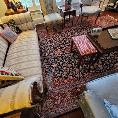 Large Persian-style area rug featuring an intricate floral pattern in navy, red, and cream, shown alongside traditional upholstered...