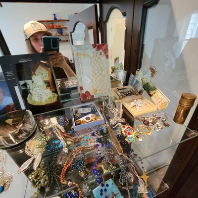 Assorted vintage and contemporary costume jewelry, rosaries, and religious items displayed on a glass shelf inside a wooden curio cabinet.