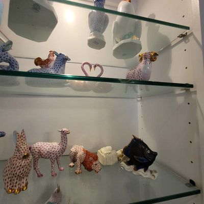 Collection of Herend porcelain figurines, including a rabbit, llama, and fish, displayed on glass shelves.
