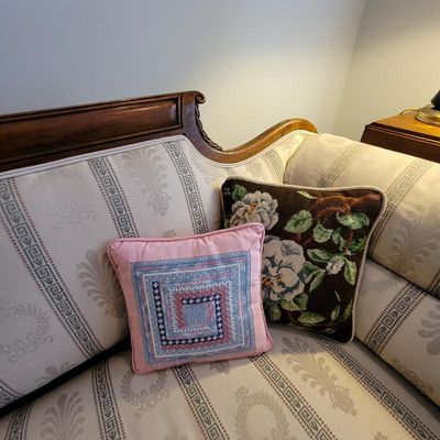 Empire-style sofa featuring striped and laurel wreath patterned upholstery, paired with two decorative throw pillows including a...
