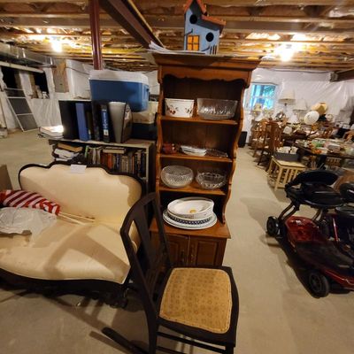 Vintage wooden hutch with open shelving displaying glassware and ceramic dishes, positioned next to a cream-colored upholstered settee...