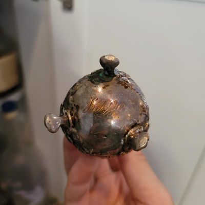 Vintage silver-plated or sterling silver three-footed vessel, showing heavy tarnish and an engraved monogram on the underside.