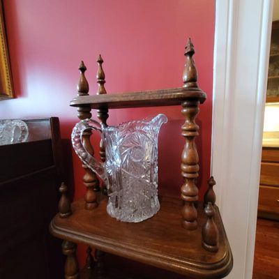 Vintage American Brilliant Period cut glass pitcher with a pinwheel pattern, displayed on a wooden tiered shelf with turned spindles.