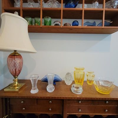 Assorted vintage glassware collection, including a pink cut-to-clear glass table lamp, yellow art glass vases, and various crystal pieces...