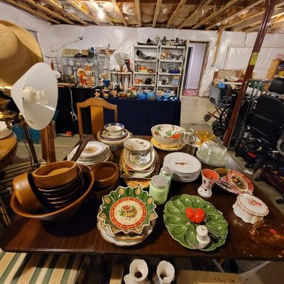 Assorted vintage tableware and kitchenware displayed on a wooden dining table, featuring wooden bowls, patterned ceramic plates, a green...