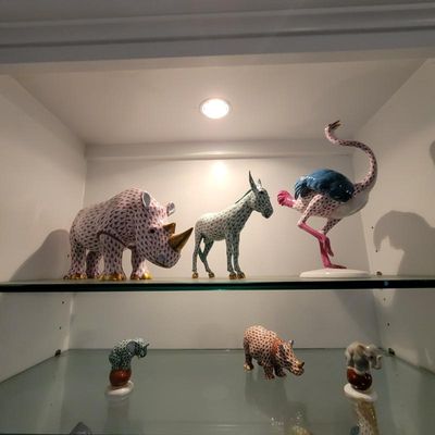 Collection of Herend porcelain animal figurines, including a large rhinoceros, donkey, and ostrich on the top shelf, and smaller elephant...