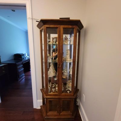 Traditional oak curio cabinet with glass shelves, mirrored back, and lower storage cabinet, filled with various ceramic figurines.