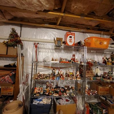 Assorted Christmas decorations and figurines, including Santa Claus statues and holiday villages, displayed on wire shelving units in a...