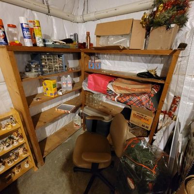 Corner wooden shelving unit holding various household items, cleaning supplies, and holiday decor, paired with a tan rolling office chair.