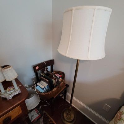 Vintage brass floor lamp with a scalloped cream fabric shade, shown alongside a wooden chair holding a basket of books.