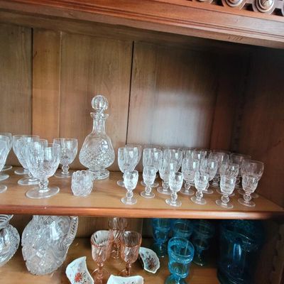 Collection of vintage cut crystal glassware, including a decanter, wine glasses, and goblets, displayed on wooden cabinet shelves.