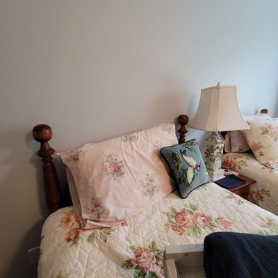 Traditional wooden twin bed frame with turned posts, dressed in floral bedding and a needlepoint bird pillow, shown alongside a matching...