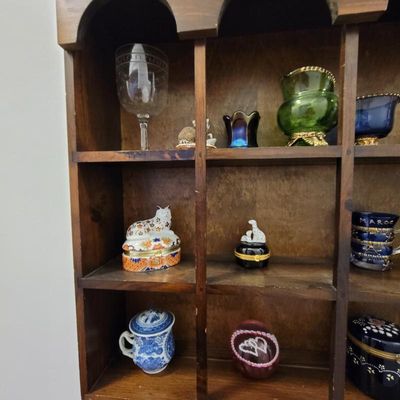 Vintage wooden shadow box shelf displaying an assortment of small collectibles, including a porcelain cat trinket box, glassware, and...