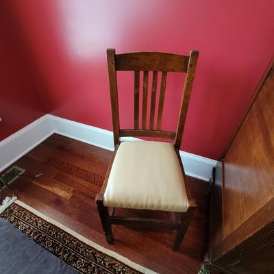 Antique Mission-style oak dining chair featuring a slatted backrest and a light beige vinyl upholstered seat cushion.