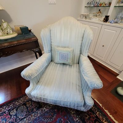 Traditional wingback armchair upholstered in a light blue and cream striped fabric, featuring a matching accent pillow.