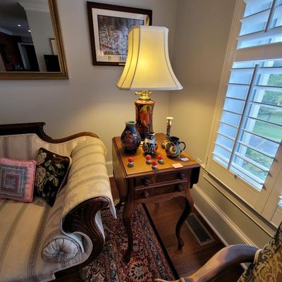 Antique wooden drop-leaf side table with cabriole legs, featuring a collection of art pottery vases and a colorful ceramic table lamp...
