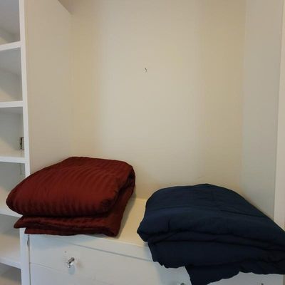 Two folded comforters, one striped burgundy and one solid navy blue, resting on a white built-in shelf.
