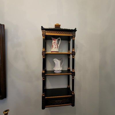 Vintage Chinoiserie-style black and gold hanging wall shelf featuring turned supports, decorative gold stenciling, and a small bottom...