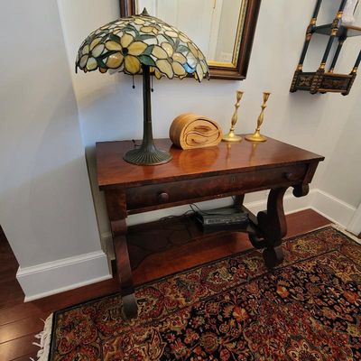 Antique mahogany console table with a single drawer and scroll legs, styled with a stained glass table lamp, a wooden jewelry box, and...