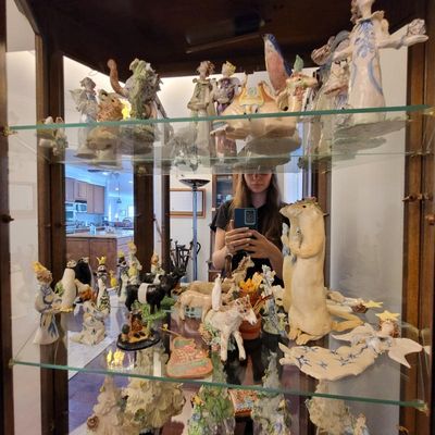 Collection of whimsical ceramic figurines, including animals and angels, displayed on glass shelves inside a wooden curio cabinet.