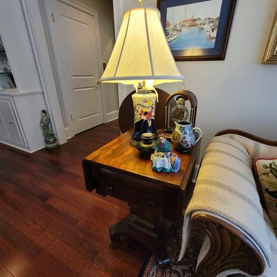 Antique mahogany drop-leaf side table featuring a hand-painted ceramic table lamp, a vintage mantel clock, and decorative porcelain...