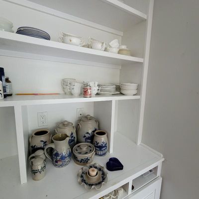 Collection of blue and white salt-glazed stoneware crocks, jugs, and pitchers displayed alongside white ceramic tableware on a built-in...