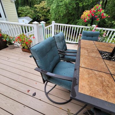Outdoor dining set featuring a tile-top table and swivel chairs with teal cushions, situated on a wooden deck.